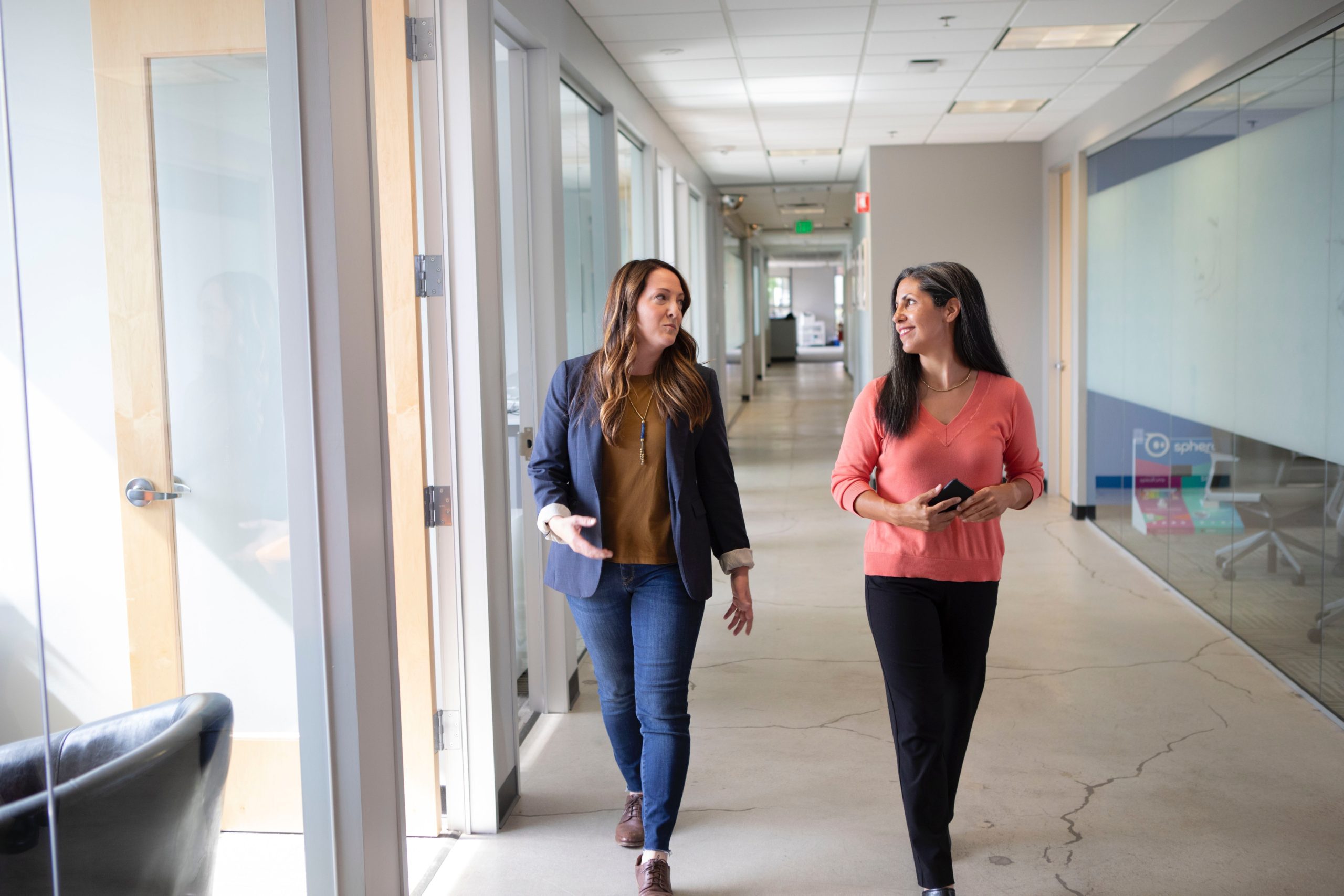 two women walking down an office hallway talking to each other