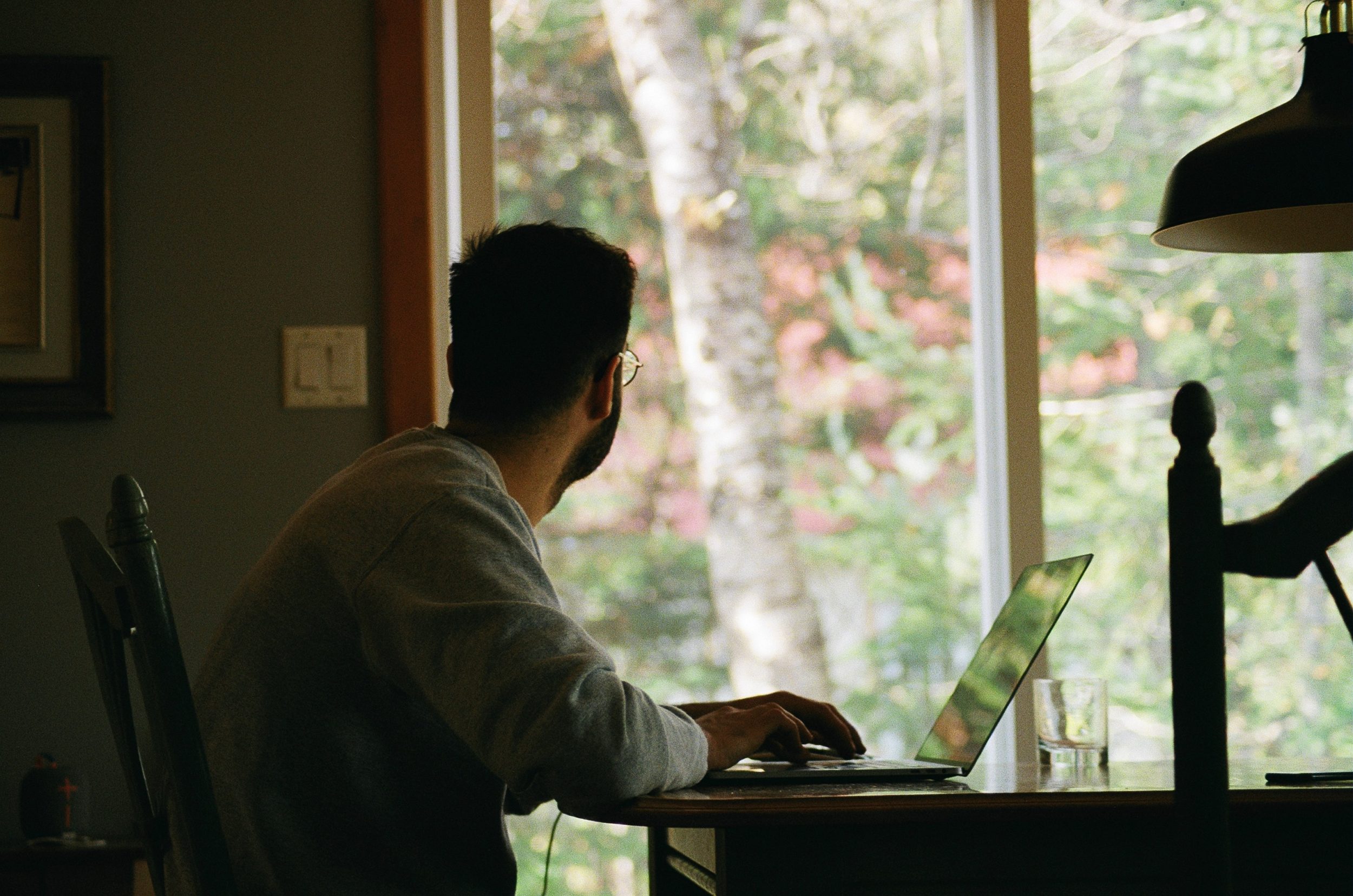 man at desk looking out of window to his backyard, home office