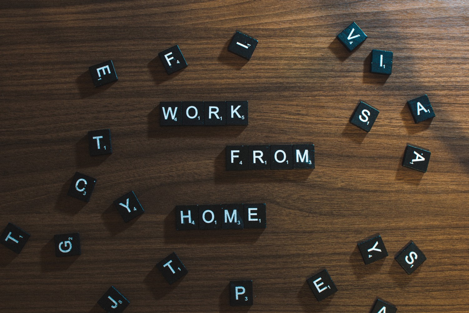 black and white Scrabble letters on a brown table spelling "work from home."