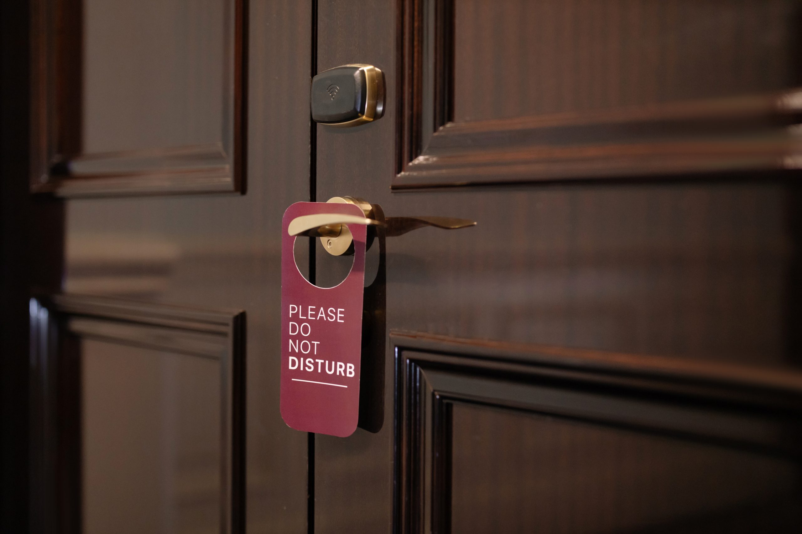 burgundy colored "Do Not Disturb" sign hanging on the handle of dark wooden doors.